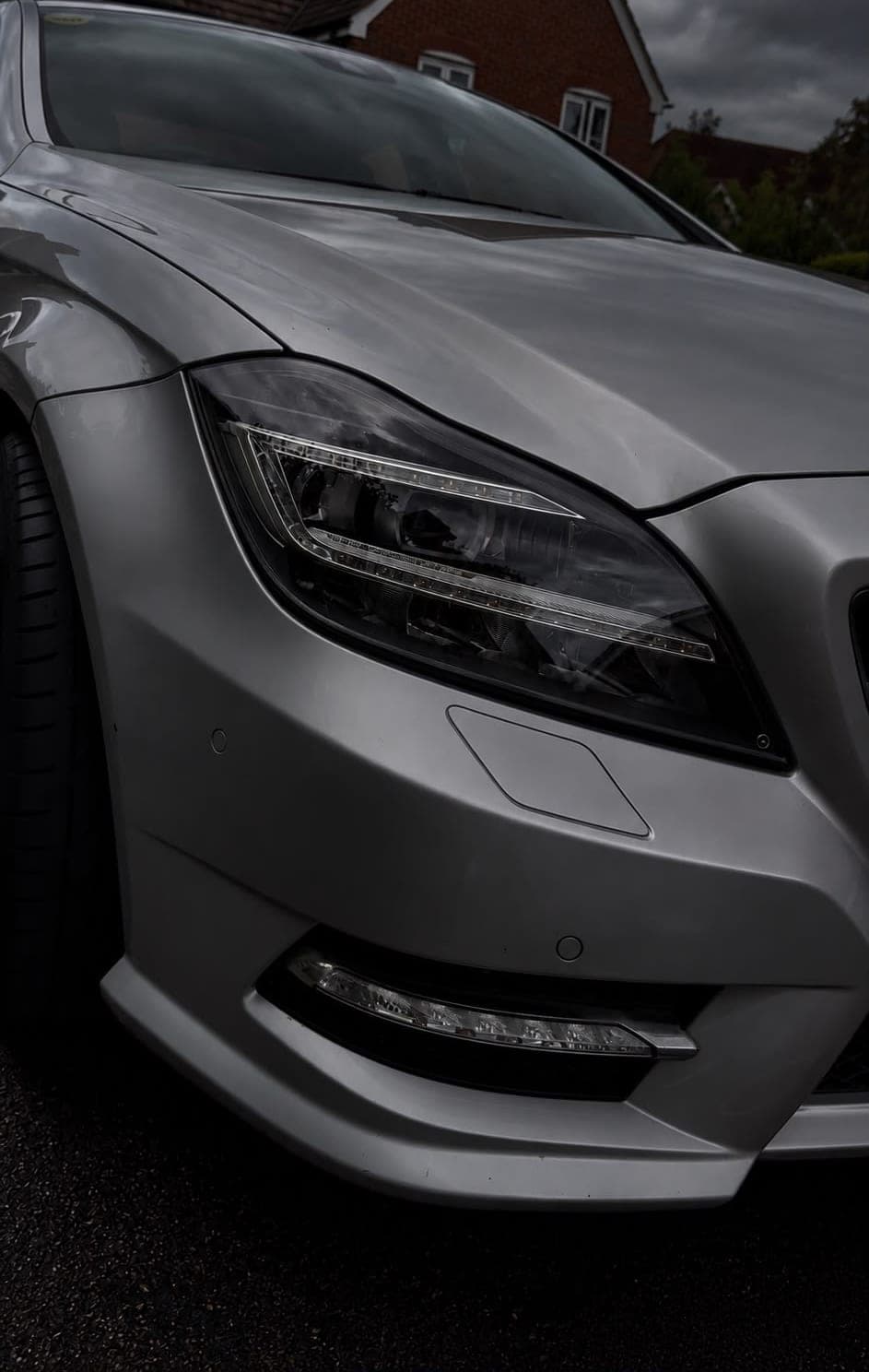 Headlight and front wing of a freshly valeted silver Mercedes CLS